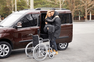 Young man helping handicapped woman to sit in wheelchair
