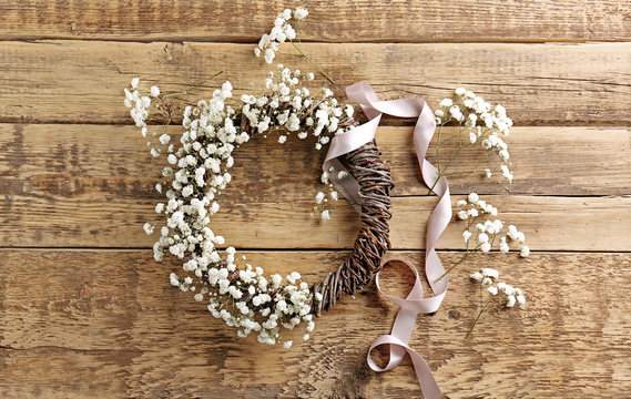 Beautiful floral wreath with satin ribbon on wooden background
