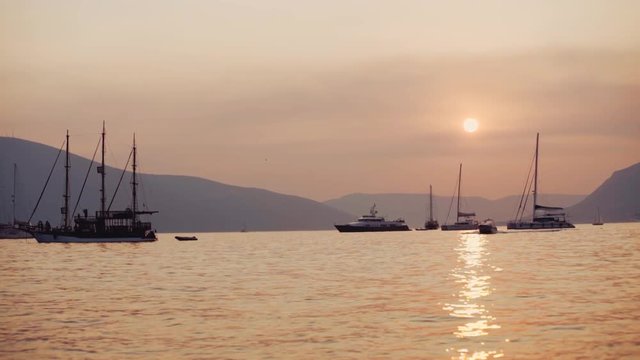 Beautiful view of the sunset and peaceful sea surface, several boats, yachts and mountain hills on the background. No people around. Romantic atmosphere, perfect scenery.