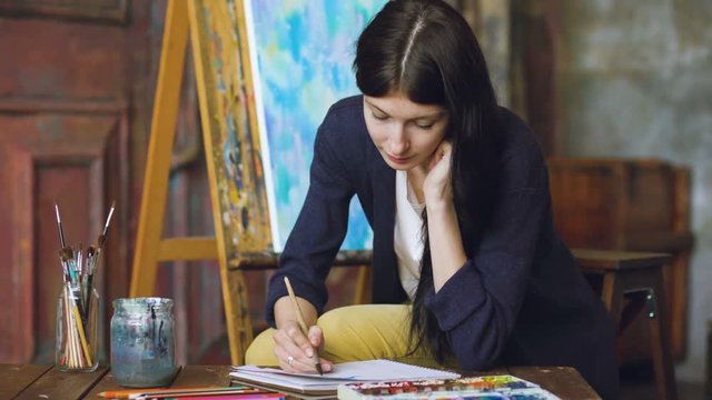 Young woman artist draw pictrure with watercolor paints and brush on easel canvas