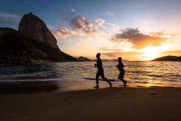 Silhouettes of Two Men Running in the Beach by Sunrise with the Sugarloaf Mountain in the Horizon