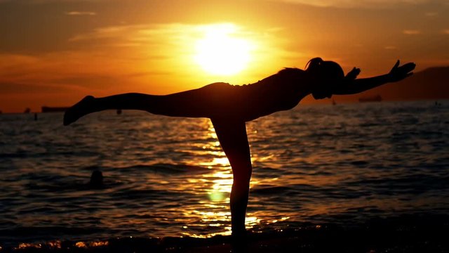 Woman performing yoga on the beach at dusk