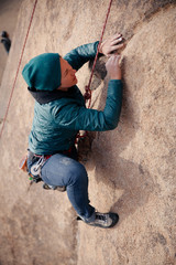 Young caucasian woman dressed for cold weather rock climbing in the desert climbs a cliff