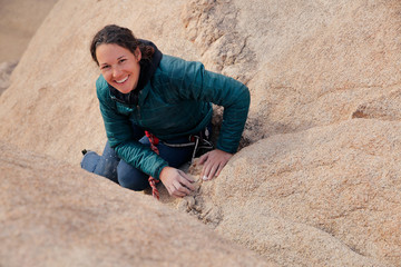Young caucasian woman dressed for cold weather rock climbing in the desert climbs a cliff and...