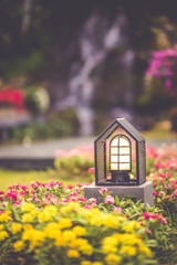 Bollard light in a beautiful colorful flowers green garden scenery background in a vertical picture vintage style.
