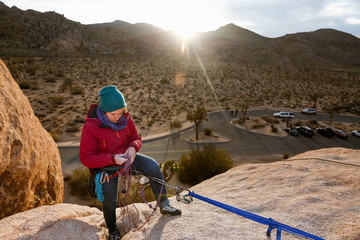 Young caucasian woman dressed for cold weather rock climbing in the desert adjusts her climbing ropes at sunset