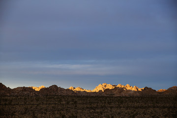 Sunset light illuminates the granite rock piles in the California desert. Joshua Trees and a winding road are also in the shot