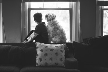 Young boy sits in the window with his dog.