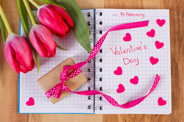 Valentines Day written in notebook, fresh tulips, wrapped gift and hearts, decoration for Valentines