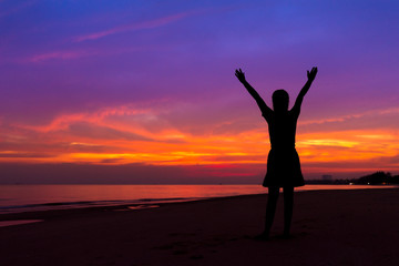 Fototapeta premium Silhouette of woman with hands up while standing on sea beach at