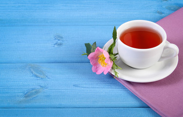 Cup of tea and wild rose flower on blue boards, copy space for text