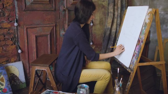 Young woman artist draw scetch wit pencil on easel canvas, preparing to paint picture