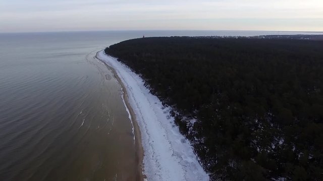 aerial footage of drone flying over frozen beach and open sea with waves crushing