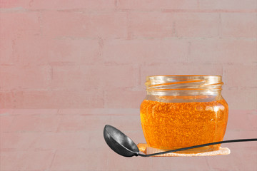 Gold yellow honey in glass jar and vintage dessert spoon on brick background. Closeup. Copy space.