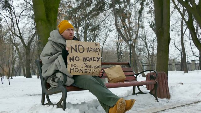
4K. Adult  homeless poor man with cardboard,   sit on  winter city bench
