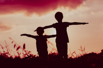 little boy and girl silhouettes play at sunset