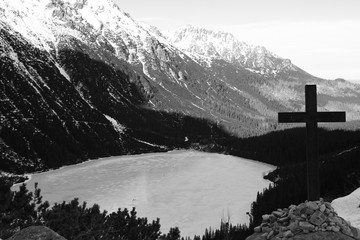 Black and white panorama of a mountain lake with a cross in the foreground