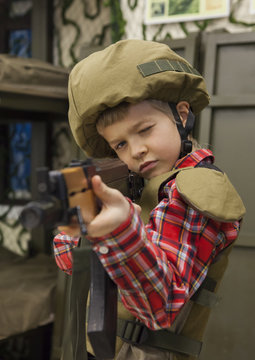 young boy in military uniform with riffle takes aim 