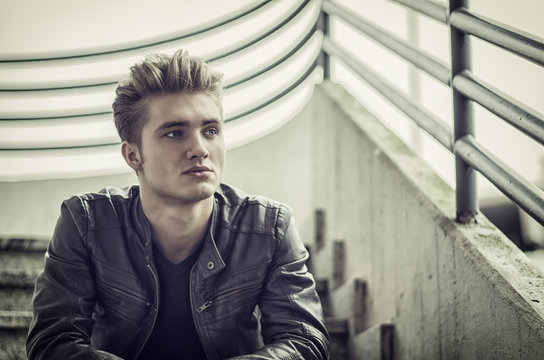 Attractive blond young man, sitting on stairs outdoors looking in camera