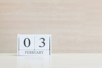 Closeup surface white wooden calendar with black 3 february word on blurred brown wood desk and wood wall textured background with copy space in selective focus at the calendar