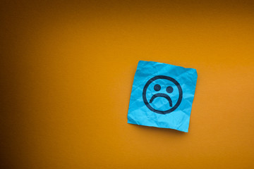 Blue paper note with sad face on a yellow paper background