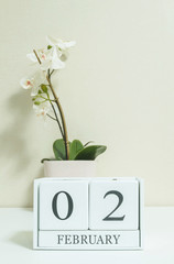 Closeup white wooden calendar with black 2 february word with white orchid flower on white wood desk and cream color wallpaper in room textured background , selective focus at the calendar