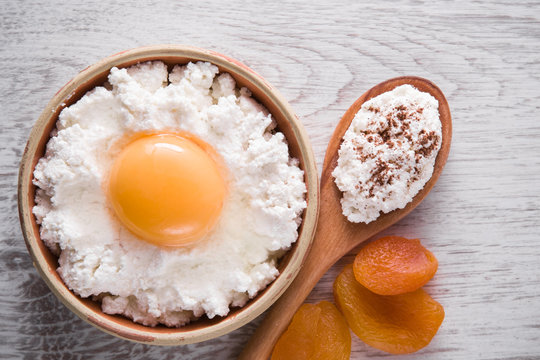 Cottage cheese and egg in the dish on the wooden table in the kitchen is not ready for frying. There more need semolina. Tasty, sweet meal with cinnamon and apricots. Healthy eating and lifestyle.