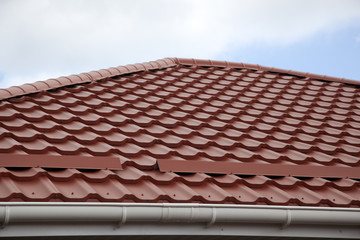 Red metal tile roof of a house against blue sky background