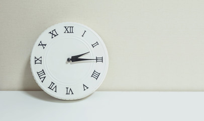Closeup white clock for decorate show a quarter past two p.m. or 2:15 p.m. on white wood desk and cream wallpaper textured background with copy space