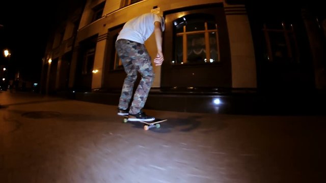 A professional skateboarder rides and doing a difficult trick on a night street