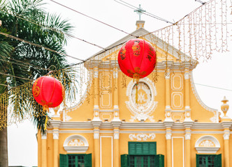 Red Chinese lantern garlands used as decorations during Chinese New year celebration in Macao city hang outdoors on yellow building background