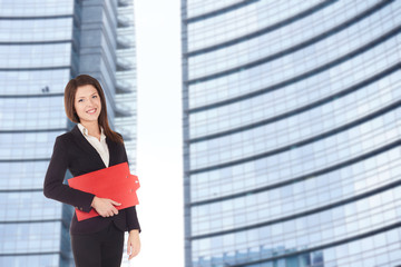 Fototapeta premium Young businesswoman with clipboard in front of office building