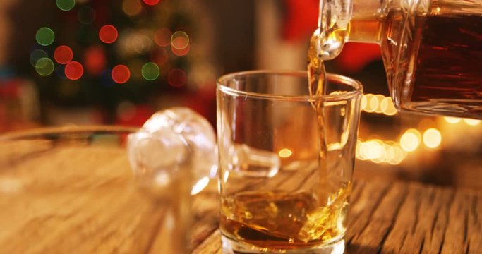 Whisky pouring into glass on wooden table during christmas time 4k