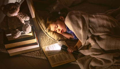 child girl sleeping in tent with  book and flashlight - obrazy, fototapety, plakaty