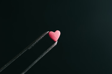 Small sugar heart in metal tweezers on dark background