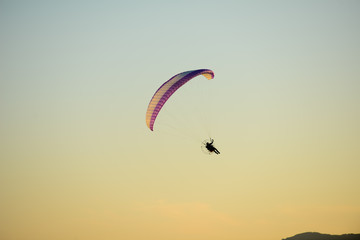 paramotor glider flying in the sky over beautiful countryside field landscape at sunset