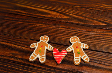 Two handmade cookie in the shape of men and heart in the middle between them on the rough wooden brown background
