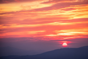 Red sunset in the mountains landscape with sunny beams. Dramatic scene.