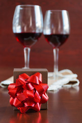 Two glasses of wine on a wooden table. Brown box with a bow.