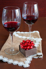 Two glasses of wine on a wooden table. Brown box with a bow.