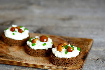 Open sandwiches on a wooden board. Sandwiches with rye bread, soft cheese, mushrooms and green onions. Wooden background with copy space for text