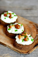 Small open sandwiches on a wooden board. Sandwiches with rye bread, soft cheese, canned mushrooms and green onions. Wooden background. Vertical photo. Closeup