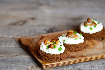 Delicious open sandwiches. Sandwiches cooked with rye bread, soft cheese, canned mushrooms and green onions. Quick appetizer recipe. Wooden background
