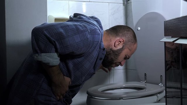  young man with beard vomits abundantly in the bathroom