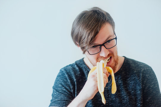 man with a beard wearing glasses eating  banana
