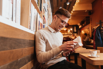 Happy man sitting in cafe while reading book