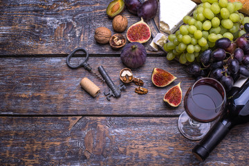 Red wine in a bottle, cork, bottle screw and a set of products - cheese, grapes, nuts, olives, figs on a wooden board, background