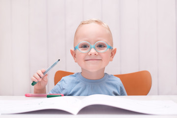 Emotional child wearing glasses sitting at the table and draws felt-tip pens