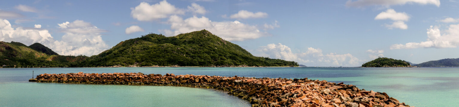 Large panorama of a tropical island taken from the coast with a jetty made of stones, Praslin Island, Seychelles