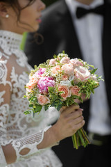 Wedding bouquet made of beige roses and pink peonies held by bri